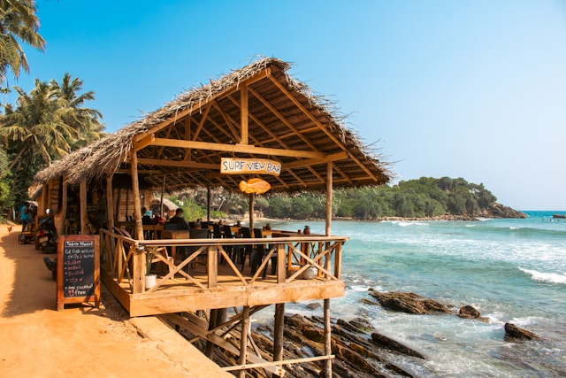 A bamboo-style hut restuarant on the edge of a beach, casting over the water.